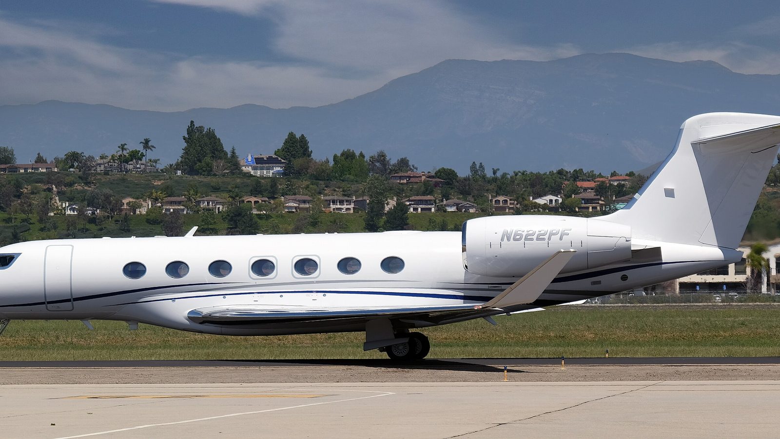 White Gulfstream G600 on a taxiway, hills and houses behind