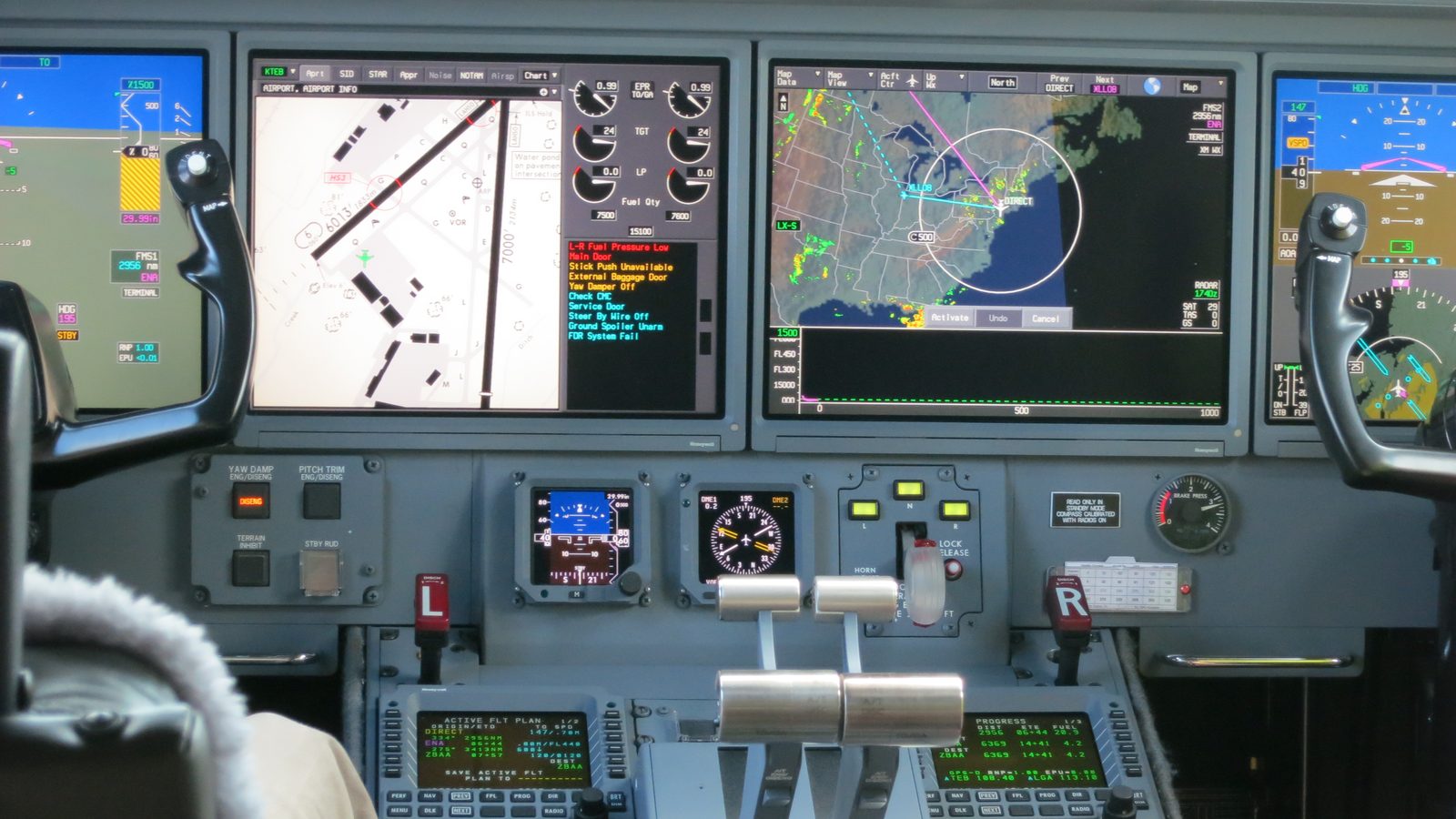 Gulfstream G550 flight deck with four screens, two yokes and thrust levers, a pilot's knees at the left seat