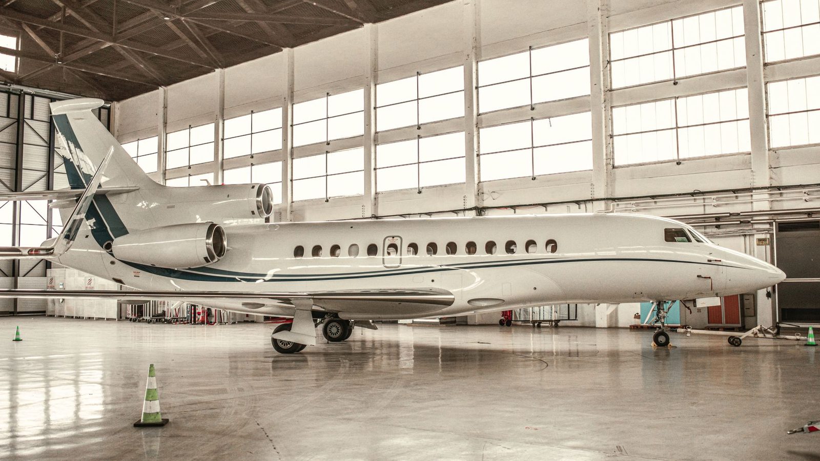 White large-cabin trijet business jet parked in a hangar