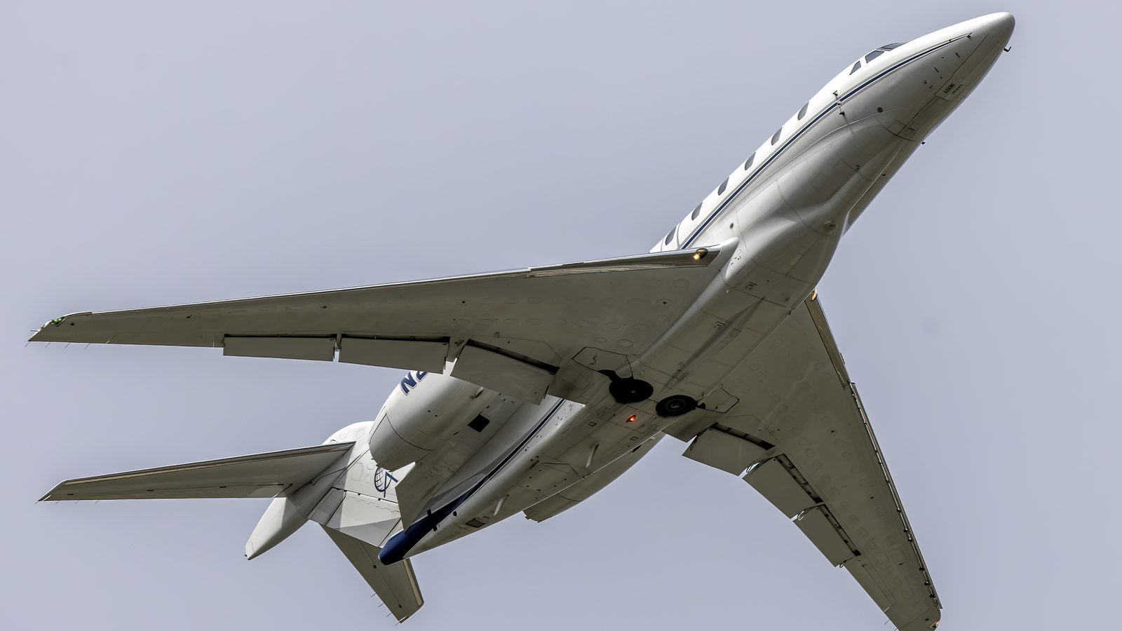 White Cessna Citation X seen from below after takeoff, two rear engines and a T-tail against a grey sky