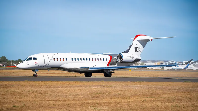 A white Dassault Falcon 10X prototype with 10X on the tail, taxiing on a dry grass-edged runway under a clear blue sky