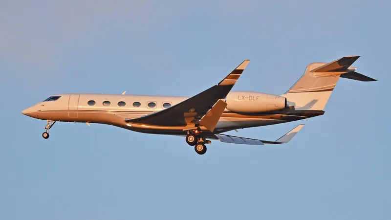 A beige Gulfstream G650 on approach against a clear blue sky, gear down, two rear engines