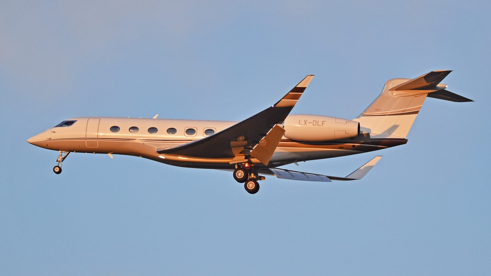 A beige Gulfstream G650 on approach against a clear blue sky, gear down, two rear engines
