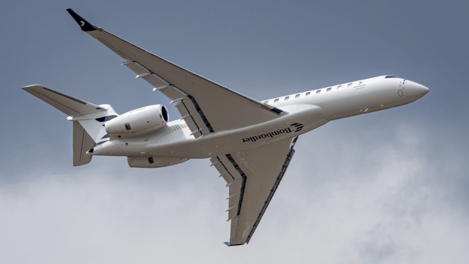A white Bombardier Global 8000 climbing against a grey cloudy sky, Bombardier titles on the fuselage