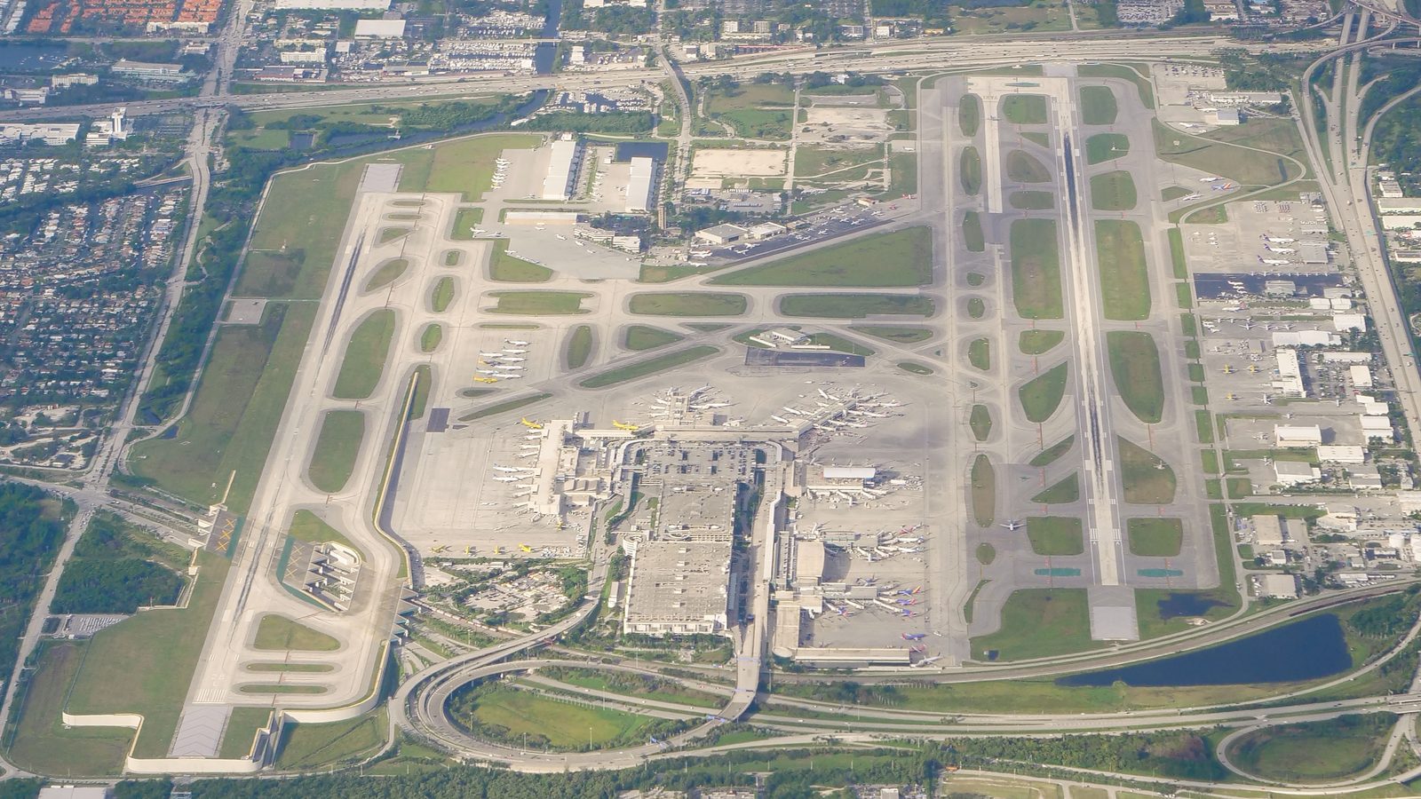 Aerial view of Fort Lauderdale-Hollywood International Airport, two parallel runways, terminals and airliners on the stands, houses and highways around the field