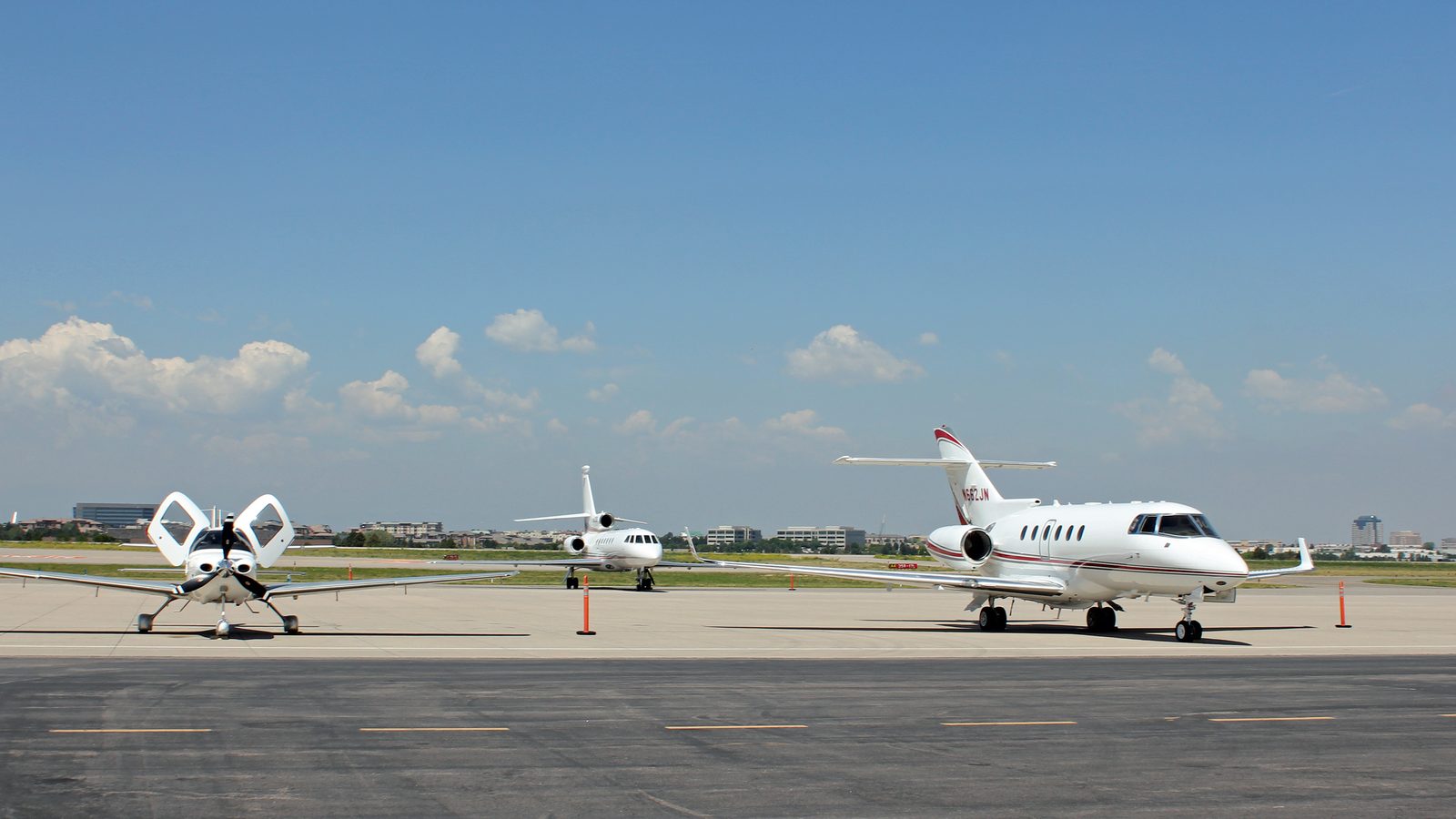 A white midsize business jet and a light twin parked on the apron at Centennial Airport, blue sky behind